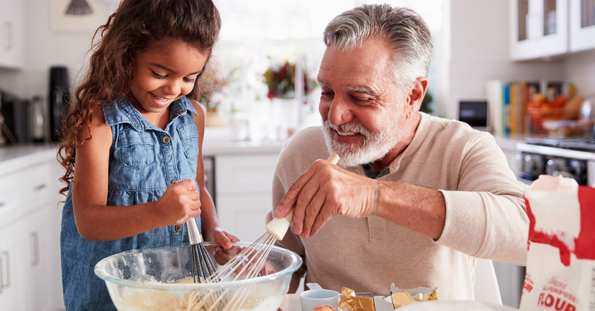 A small child and her grandfather stir batter in a bowl. 