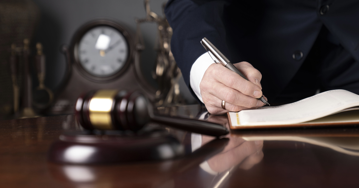 A closeup image of a businessman's hand, working diligently in an office setting, utilizing pen and computer technology.