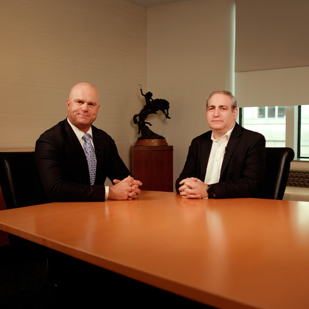 Two businessmen in a modern office setting, seated at a desk with a computer, engaged in a professional discussion.