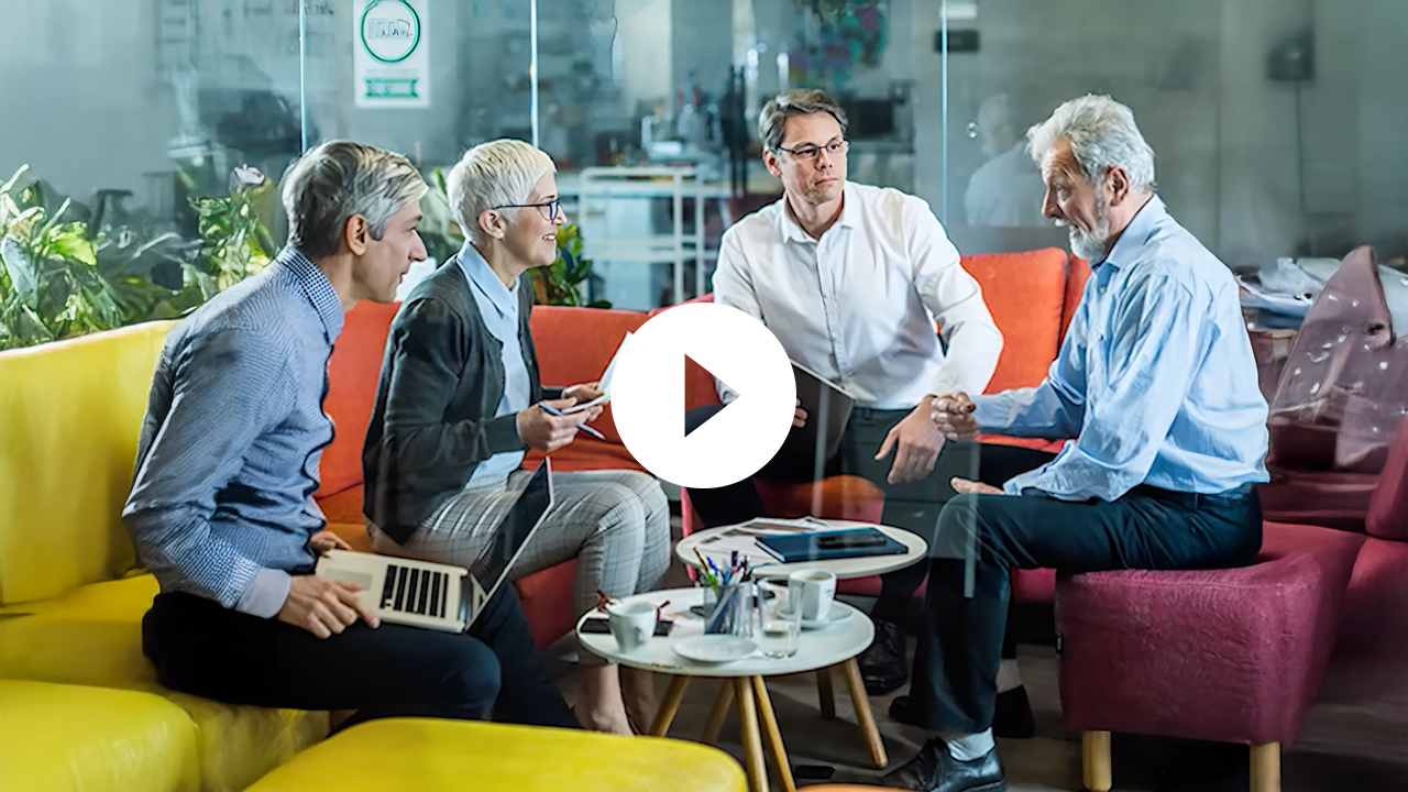 A senior businessman and businesswoman engage in a professional discussion, exchanging ideas in a positive, collaborative setting.