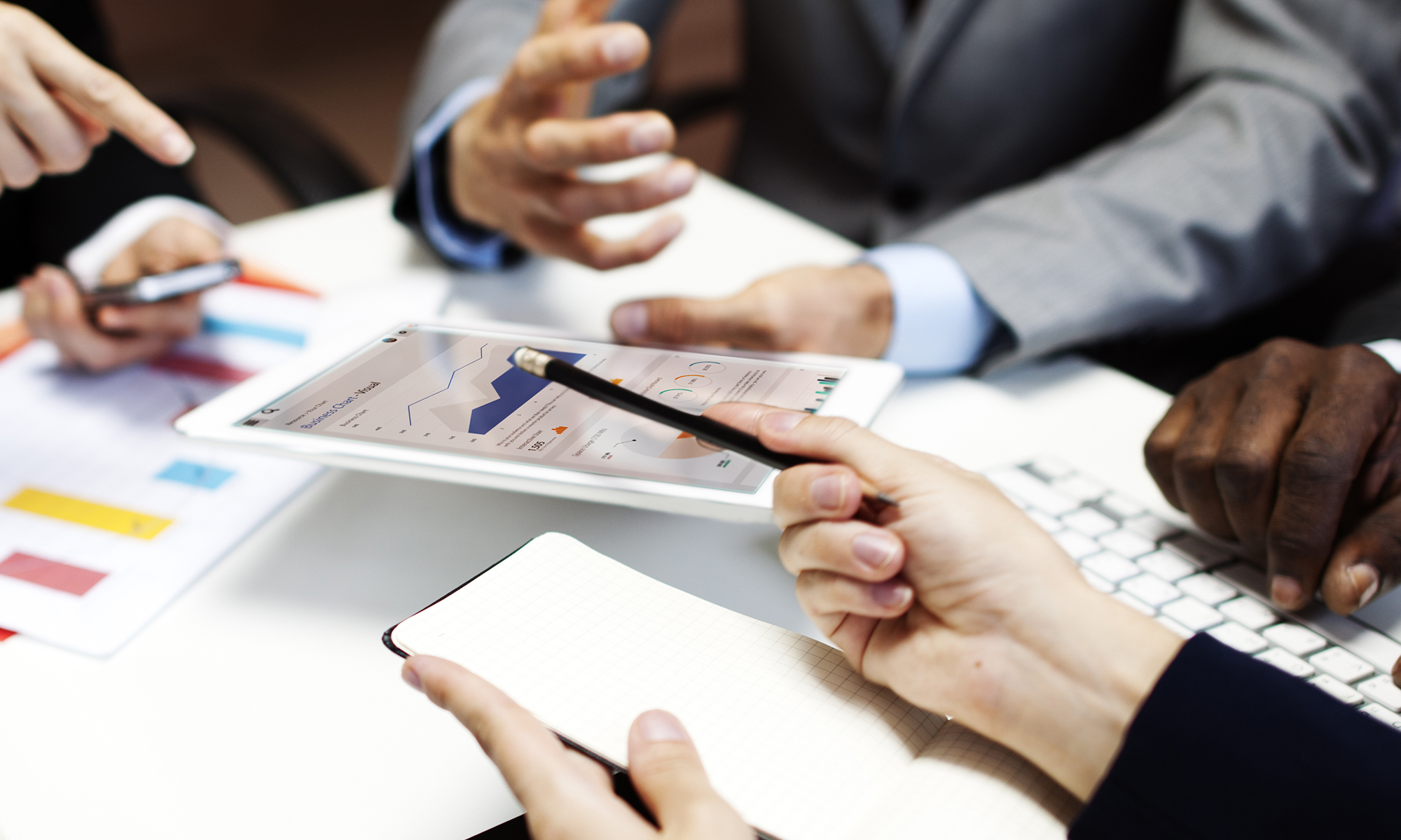 Several people collaborating around a table, reviewing financial charts and dashboards displayed on a tablet and printed reports.