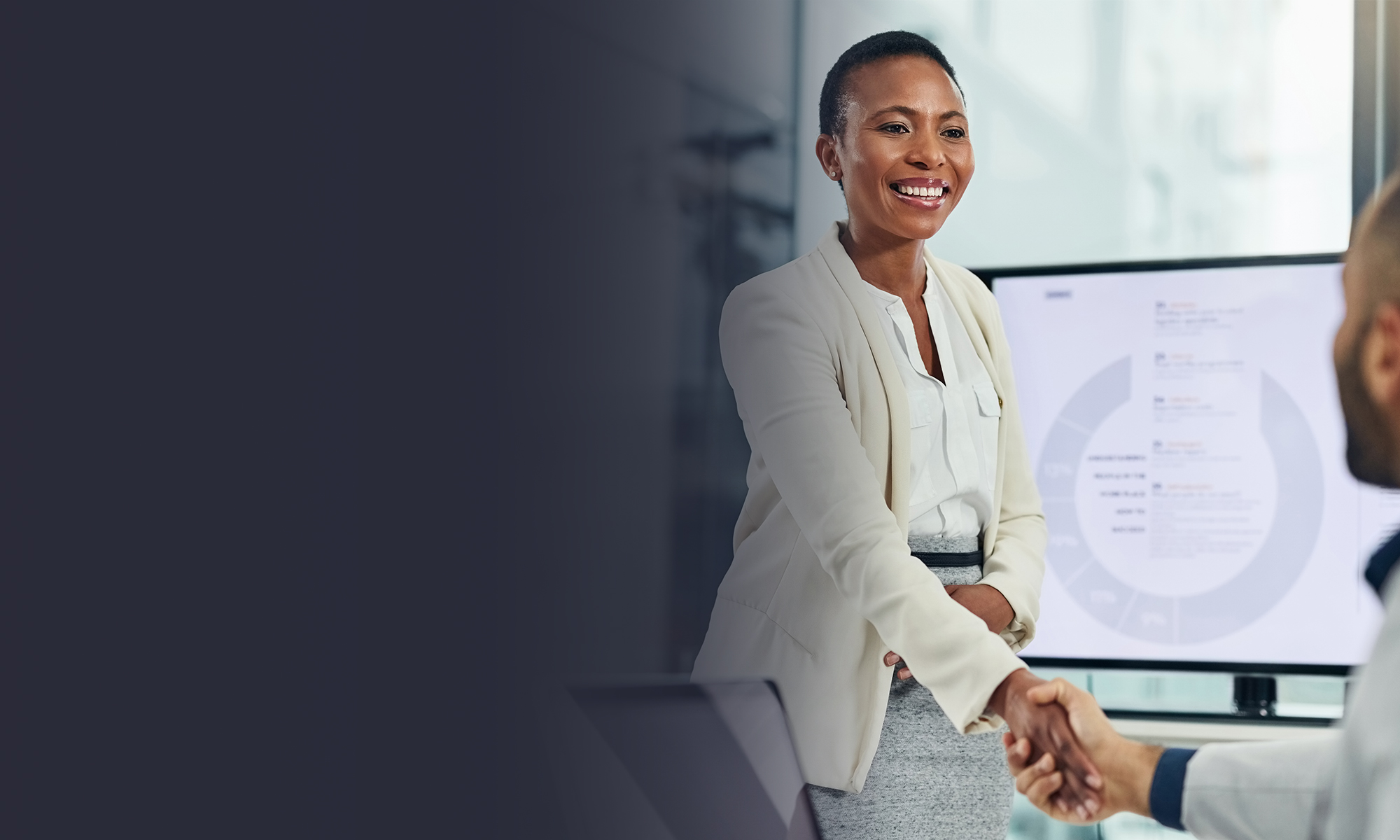 Professional shaking hands with a client during a business meeting, with a presentation screen visible in the background.