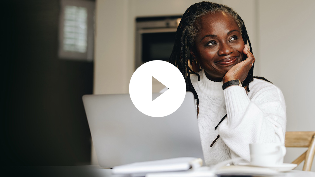 A smiling businesswoman works on a laptop in a professional office setting, surrounded by colleagues in a collaborative environment.