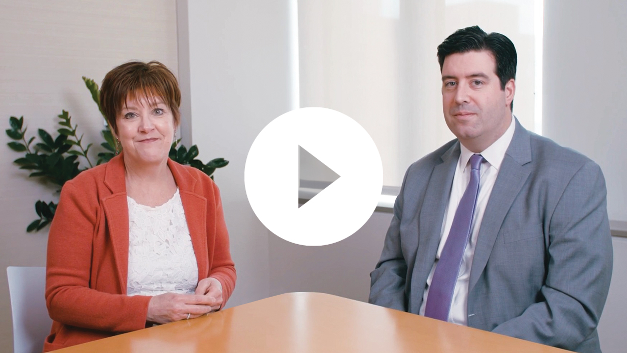 A professional man and woman collaborate in a modern office setting, working on a project using a laptop.