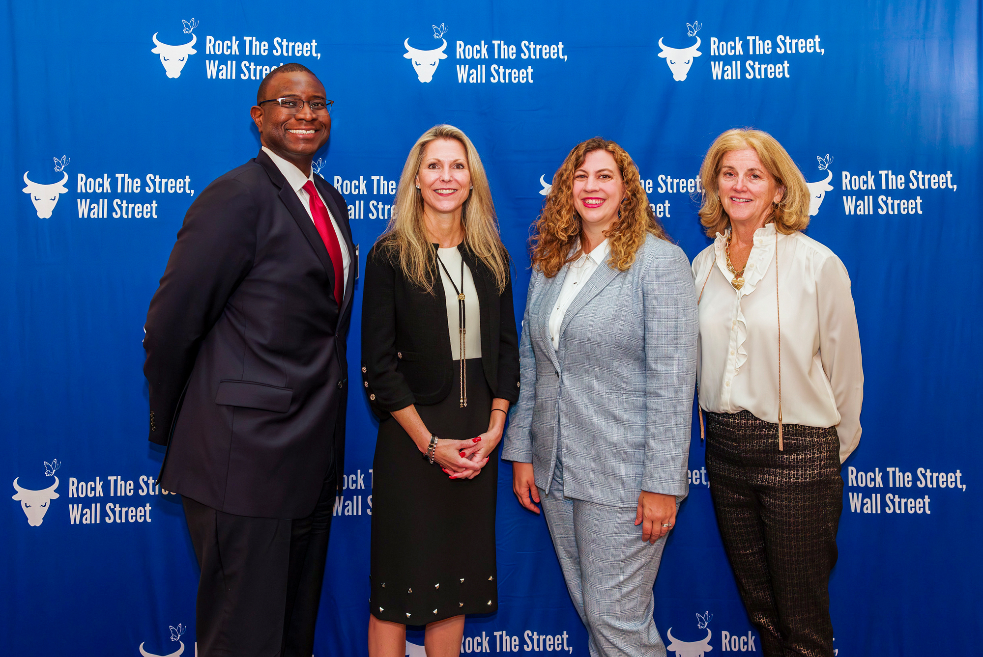 Group of four individuals posing in front of a Rock The Street, Wall Street step-and-repeat backdrop at an event