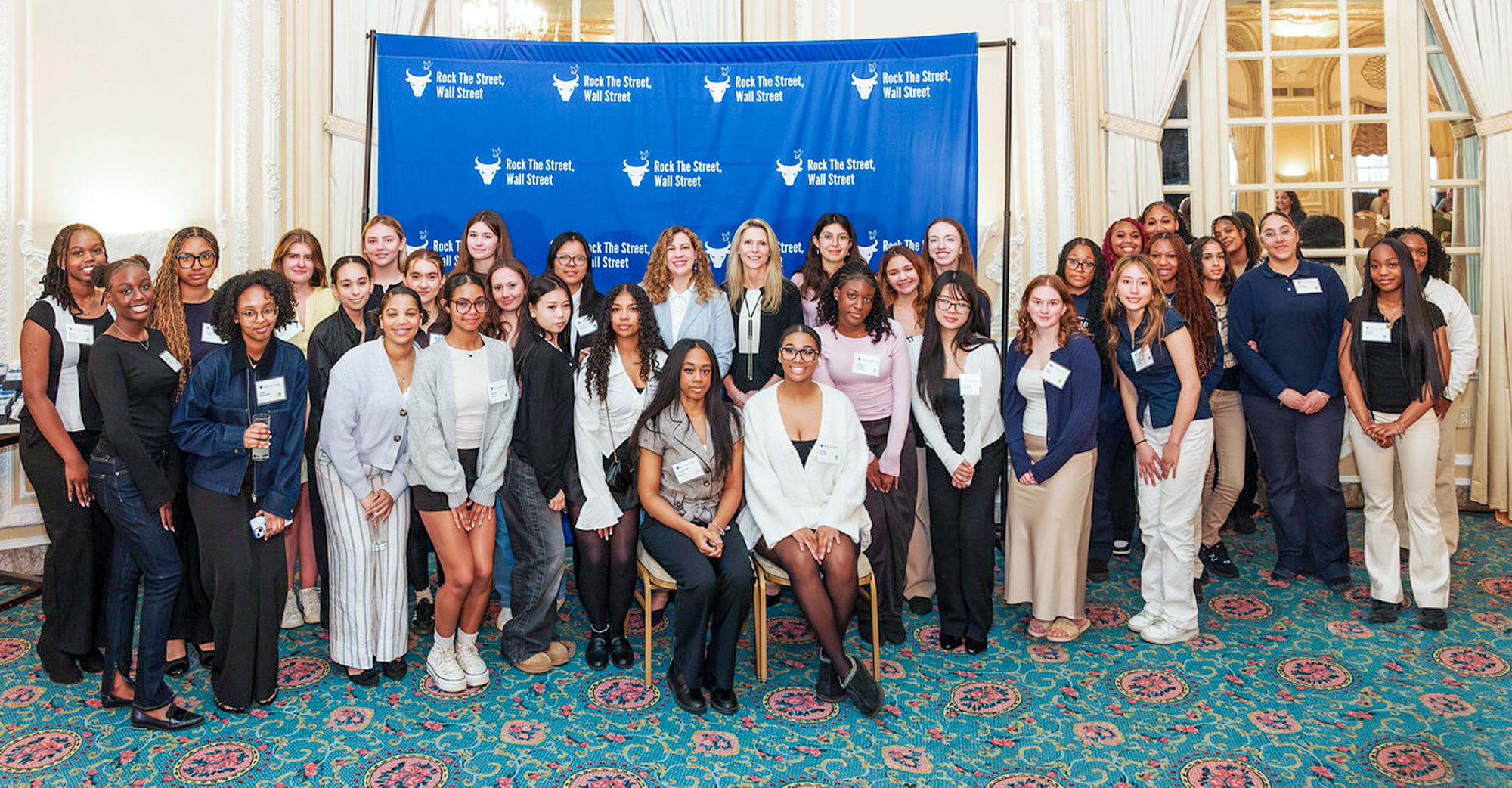 Group of students posing with event leaders in front of a Rock The Street, Wall Street backdrop