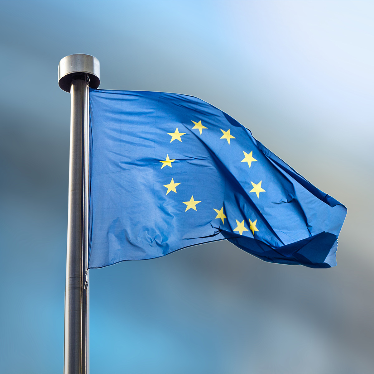 The flag of the European Union, embellished with stars, flutters against the vibrant blue sky, symbolizing unity in Europe.
