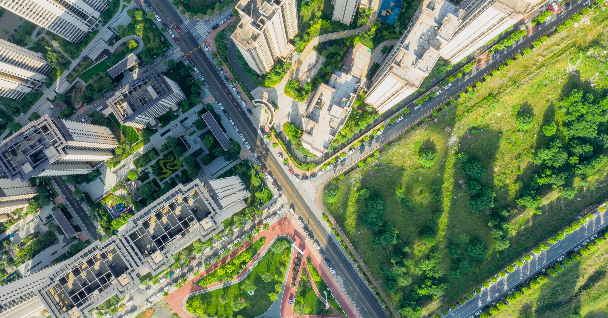 Aerial view of four streets intersecting, with an urban landscape (skyscrapers, etc.) on one side of the divide and a more rural setting (trees, fields, etc.) on the other side